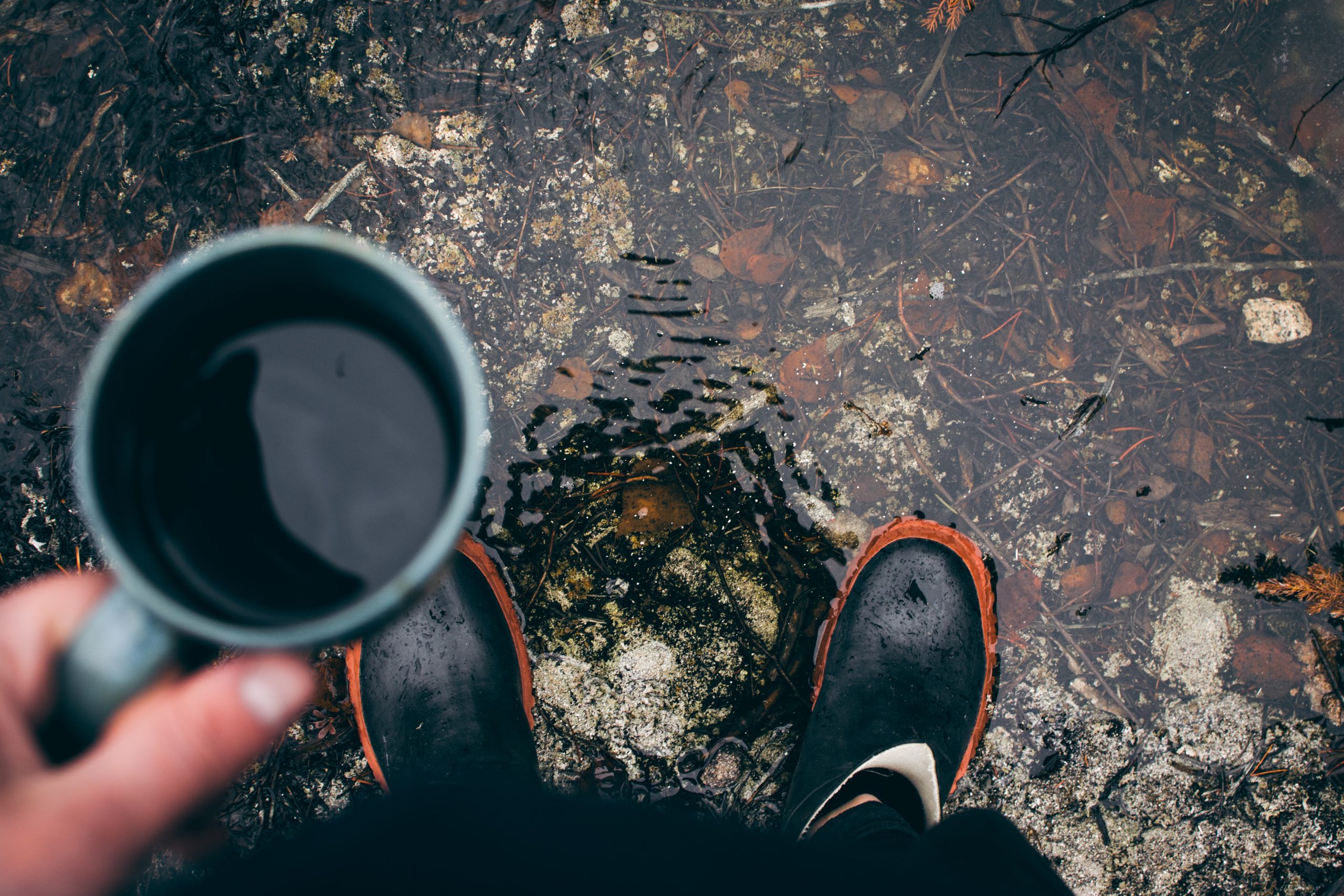 a man standing on a water puddle with a cup of coffee in his hand